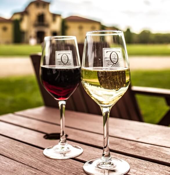 Eat & Drink Two glasses of wine — one red, one white — sit atop a wooden table outside of a vineyard in Beloit, WI.